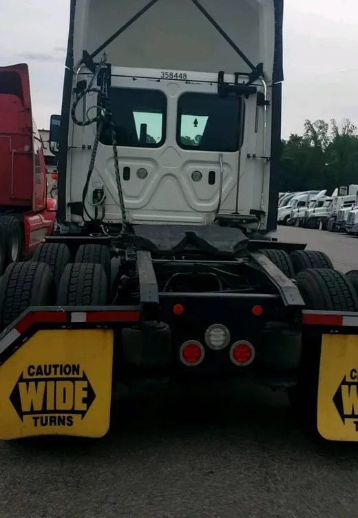 Rear of a white day-cab tractor parked in a carrier yard, mud flaps reading Caution Wide Turns, other tractors lined up behind
